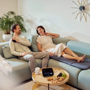 A man and woman relaxing on a sofa using BEMER® therapy products.